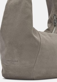 Szara zamszowa torba o miękkiej fakturze, o unikalnym zaokrąglonym kształcie i zamknięciu na zamek. Posiada wytłoczony logo marki po boku.