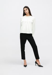 Hvid bluse med lange ærmer og samlet hals, kombineret med sorte smalle bukser og spidse sorte hæle. Glat stoftekstur, minimalistisk design.