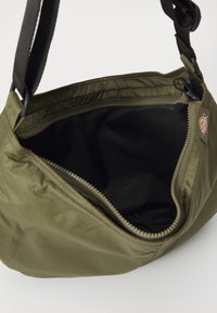 Zelena tkanina ramenska torba z zadrgo, notranjost je črna, nastavljiv trak. Vidna oznaka blagovne znamke na strani.