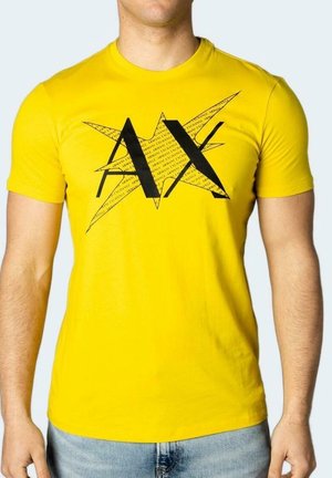 T-shirt jaune en coton, présentant un motif graphique noir avec "AX" et des éléments en forme d'étoile. Manches courtes, col rond, coupe ajustée.