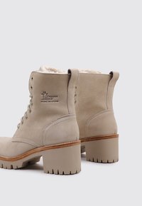 Beige Ankle Boots mit Wildleder-Oberfläche und Kunstfell-Futter, ausgestattet mit einem gestapelten Absatz, runder Spitze und Metallösen für die Schnürsenkel.