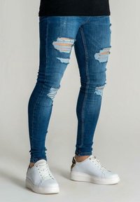 Jaansit venytetyt siniset, joissa on useita repeämiä polvissa. Yhdistettynä valkoisiin matalavartisiin tennareihin ja mustaan paitaan.