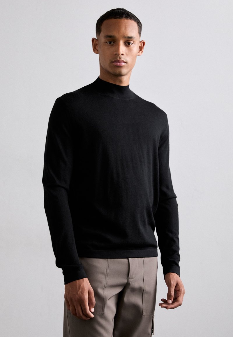 Schwarzer Pullover mit langen Ärmeln, hohem Kragen und taillierter Passform, aus glattem Stoff. Verfügt über minimale Nähte und schmal zulaufende Bündchen.
