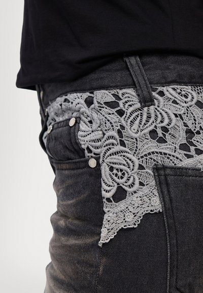 Höga svarta denimjeans med en grå spetsmidja med blommönster och dekorativ hårdvara.