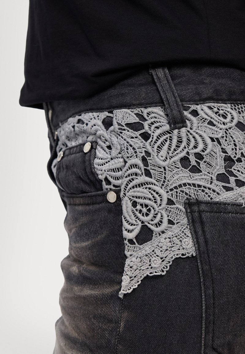 Zwarte denim jeans met hoge taille, voorzien van een grijze kant tailleband met bloemenpatronen en decoratieve hardware.