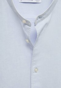 Camicia di lino azzurro chiaro con colletto alla mandarina alto, dotata di due bottoni trasparenti all'apertura del collo e una consistenza morbida.