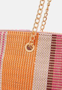Dzianinowa torba typu tote z żywymi wzorami w kolorze pomarańczowym, różowym i beżowym. Złoty łańcuszkowy pasek i okrągłe, złote okucia podkreślają design. Teksturowana powierzchnia.