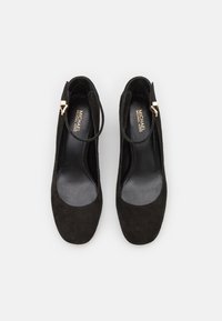 Zapatos de tacón alto de ante negro con puntera redondeada, correa en el tobillo y detalles de hardware dorado. El forro interior suave contrasta con la textura exterior.