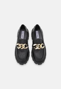 Schwarze Leder-Pantoletten mit dicken Sohlen und übergroßer goldener Kettendetailierung an der Oberseite, innen mit dem Label Steve Madden.