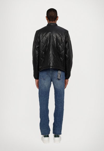 Veste en cuir noir matelassée avec un col montant ; associée à un jean en denim bleu avec une poche arrière à motif et des baskets blanches.