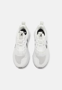 Par hvide atletiske sko med sorte chevron-logoer og trækstropper, vist side om side med spidsen opad på en hvid baggrund.