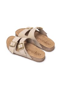 Beige suede sandals with two wide straps, featuring gold metal buckles, and a textured cork and rubber sole. Simple design with no patterns.