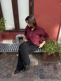 Burgundijski pulover s polovičnim zadrgo, črne široke hlače in črni škornji z ostrimi konicami. Značilna gladka tkanina in preprosti oblikovalski detajli.