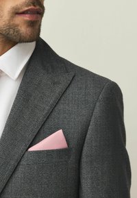 Szürke sakktáblamintás blézer bevágott hajtókákkal, fehér texturált inggel és egy rózsaszín zsebkendővel a mellzsebben.