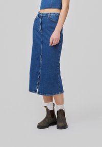 Denim midi skjørt med frontsplitt, med høy midje, blå vask, klassiske sømmer, og brukt med brune ankelstøvler og hvite sokker.