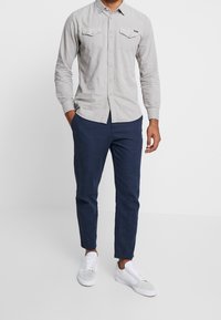 Maglietta a maniche lunghe grigia chiara con due tasche sul petto, davanti con bottoni, e pantaloni navy slim-fit. Abbinata a sneaker bianche e una texture sottile.