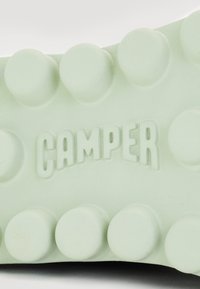 Hellgrüner Gummisohle mit erhöhten, kreisförmigen Mustern und "CAMPER" in einer fetten, modernen Schriftart in der Mitte eingraviert.