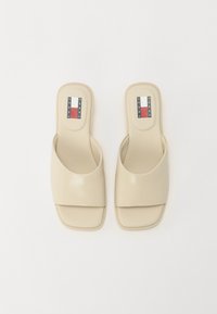 Sandales mules beige avec une finition lisse et brillante ; large bride supérieure et semelle rectangulaire ; logo de la marque sur la semelle.