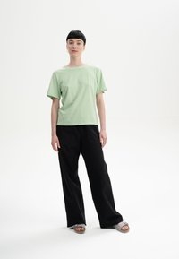 Helles grünes Kurzarm-T-Shirt, kombiniert mit schwarzen weiten Hosen und grauen Sandalen. Einfaches Design, lockere Passform, glatte Textur.