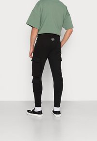 Zwarte cargojoggers met meerdere zakken en een slim-fit ontwerp. Gecombineerd met een losse groene t-shirt en zwarte sneakers met witte zolen.