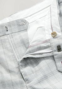 Pantalon à carreaux gris clair avec doublure intérieure blanche, braguette à glissière partiellement ouverte, bouton et crochets métalliques visibles à la taille.