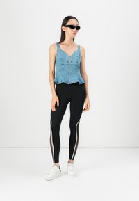 Denim peplum top with a front zipper, black leggings featuring mesh side panels and white stripes, paired with white sneakers.
