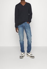 Svart långärmad V-ringad tröja, blå slim-fit jeans och svart-vita sneakers. Slät tygkvalitet med en avslappnad passform.