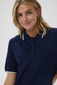 Tamsiai mėlynas polo marškinėliai su klasikiniu apykakle, turintys baltas juosteles ant apykaklės ir rankovių kraštų, pagaminti iš minkštos trikotažo medžiagos.