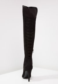 Stivale alto in suede nero con un design strutturato, dotato di tacco alto, dettaglio in pizzo sul retro e chiusura a zip sul lato.