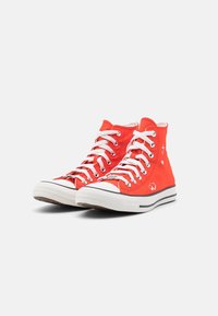 High-top sneakers made of red canvas with white rubber soles, featuring white laces, silver eyelets, and heart and star graphics.