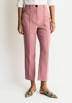 Light pink tailored pants with front pleats and a button closure, paired with snakeskin-patterned slip-on shoes. Smooth texture, ankle length.
