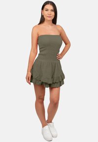Groene strapless mini-jurk met een gerimpelde top, een volantrand, gemaakt van gestructureerd materiaal, gecombineerd met witte sneakers.