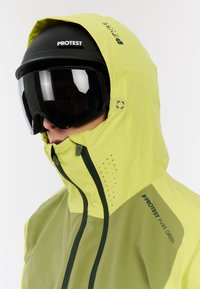 Helle grüne wasserdichte Jacke mit Kapuze, kontrastierenden dunkelgrünen Reißverschlüssen und Belüftungsöffnungen. Entwickelt für Wintersportarten.
