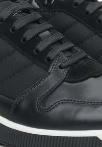 Czarne sportowe buty z połączeniem gładkiej skóry i teksturowanej tkaniny, z zapięciem na sznurowadła oraz kontrastującą białą podeszwą środkową.