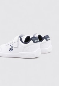 Zapatillas blancas con un acabado de cuero suave, acentos grises, correa ajustable de velcro y un detalle de logo en el costado y el talón.