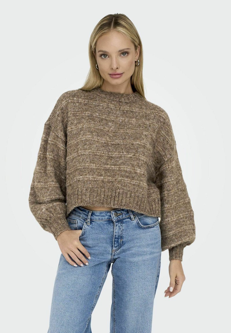 Pull en maille texturé marron avec un col montant et des manches ballons, associé à un jean droit bleu clair, au design minimaliste.