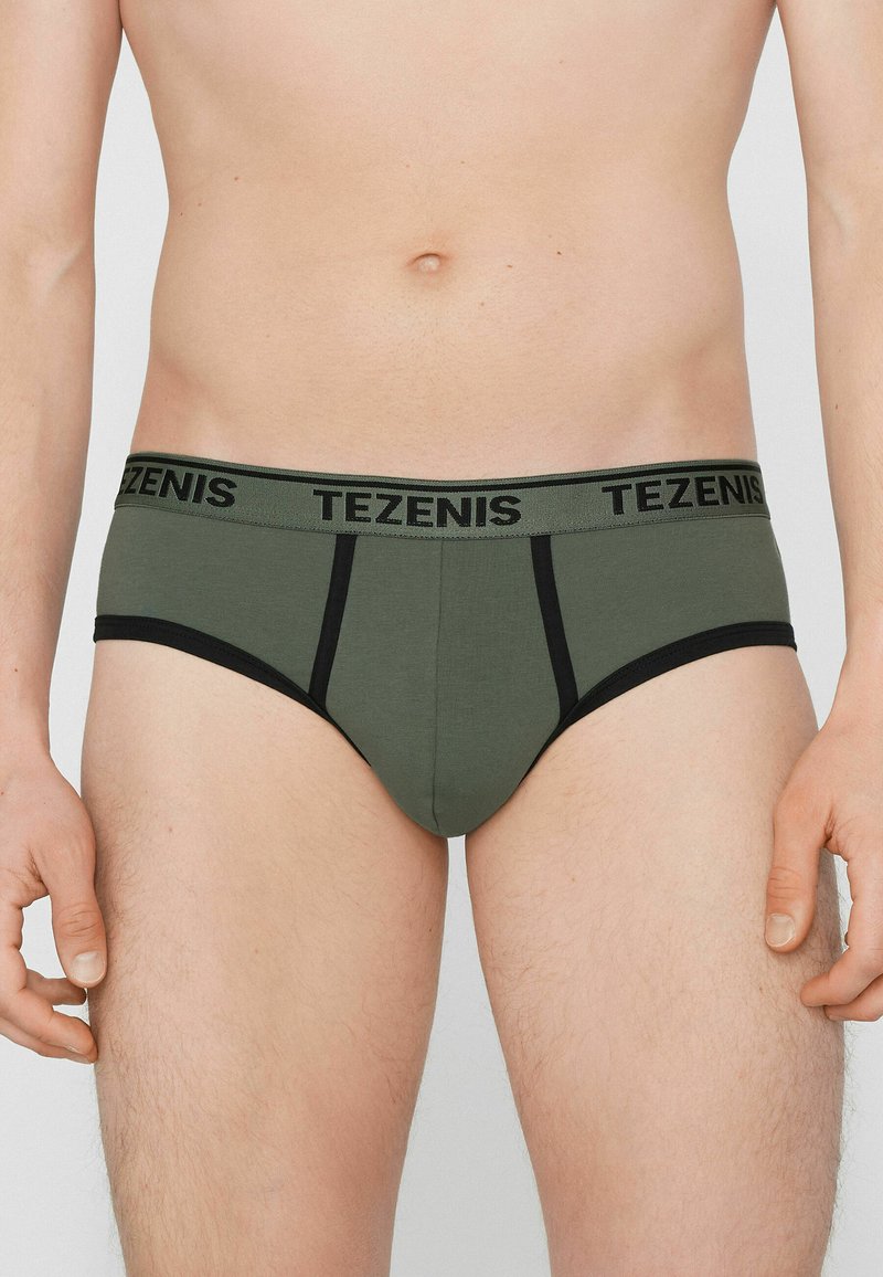 Culotte en coton vert olive avec ceinture noire, arborant le logo "TEZENIS". Le design comprend des détails cousus et des accents noirs contrastants.