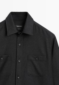 Schwarzes Hemd mit Knopfleiste aus strukturiertem Stoff. Verfügt über einen spitzen Kragen, zwei Brusttaschen und schwarze Knöpfe für den Verschluss.