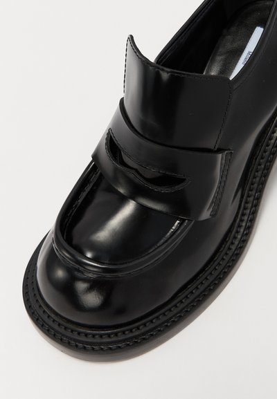 Scarpa nera in pelle con dettagli a taglio, punta arrotondata e parte anteriore rialzata. Presenta una cucitura a bordo e una superficie liscia e lucida.