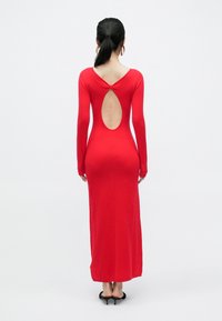 Czerwona sukienka z długim rękawem o dopasowanym kroju, z okrągłym wycięciem na plecach i prążkowaną fakturą. Gładki materiał, długość do podłogi.