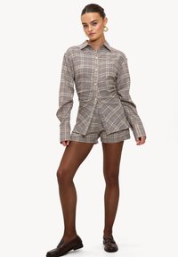 Chemise à carreaux à boutons avec short assorti ; tissu apparemment doux, couleurs beige et marron ; présente une coupe cintrée et des manches longues.