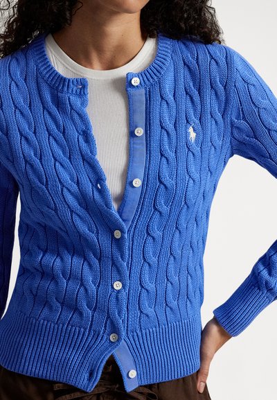 Zils kardigans ar rakstu adījumu, apaļu kakla izgriezumu, pieciem pogām, ribotām aprocēm un apakšu. Kreisajā krūšu pusē neliels logo.