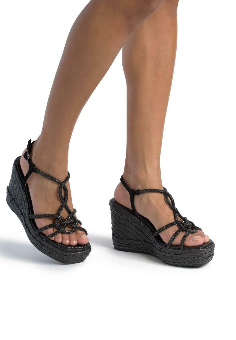 Sandalias de cuña negras con textura trenzada, que presentan un diseño con tiras. Correa en el tobillo ajustable y dedos al aire destacados.