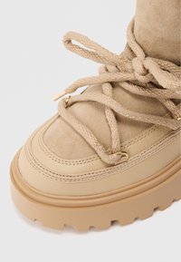 Μπεζ σουέτ μπότες με παχύ καουτσούκ πάτο, με περίπλοκη δέσιμο, χρυσές λεπτομέρειες φ�ινιρίσματος και επίπεδες ραφές.