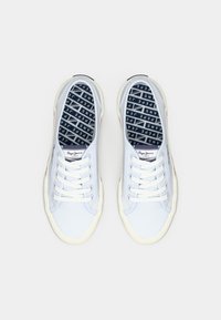 Pair of white canvas lace-up sneakers with blue and white branded insoles, viewed from above on a white background.