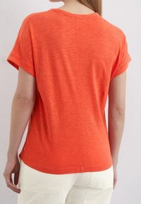 Orange kortærmet T-shirt med rund halsudskæring, der har en blød tekstur og subtil melange mønster. Sømdetaljen løber lodret.