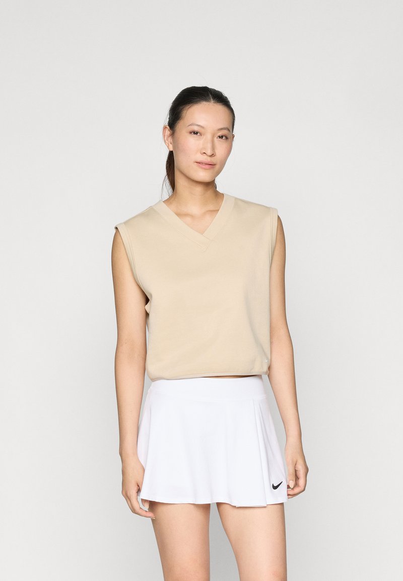 Beige mouwloos topje met een V-hals en een cropped fit, gecombineerd met een witte klokrok met een zwart Nike-logo op de zoom.