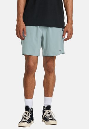 Pantaloni sportivi azzurri chiari realizzati in tessuto morbido, con un logo sulla parte anteriore, abbinati a sneakers nere alte e calze bianche.