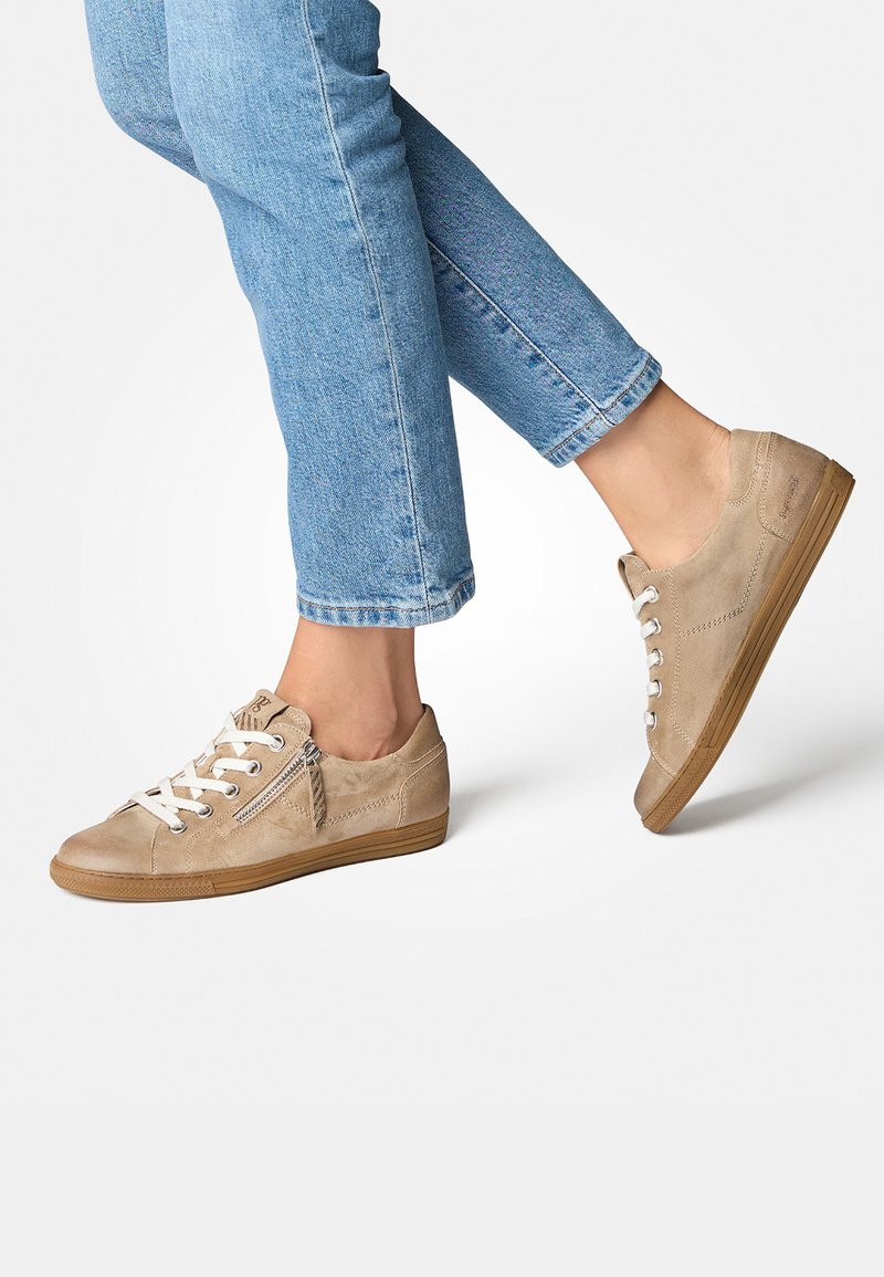Beige Wildlederschuhe mit weißen Schnürsenkeln, seitlichem Reißverschluss und brauner Gummisohle. Getragen mit hochgekrempelten blauen Jeans.