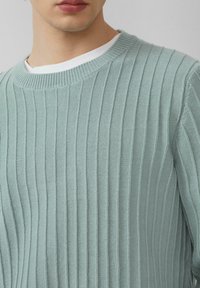 Jasnoniebieski, ribbowany sweter z okrągłym dekoltem i fakturowanym materiałem. Widać gładką białą podkoszulkę na dekolcie.